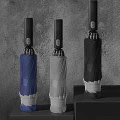 Three folded automatic umbrellas in blue, grey, and black stand upright on a dark surface.