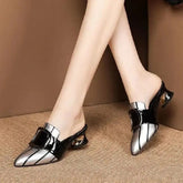 A pair of silver and black pointed-toe slip-on mules with a decorative buckle and a low block heel.