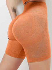 A person wears orange high-waisted seamless workout shorts with a booty-lifting design.