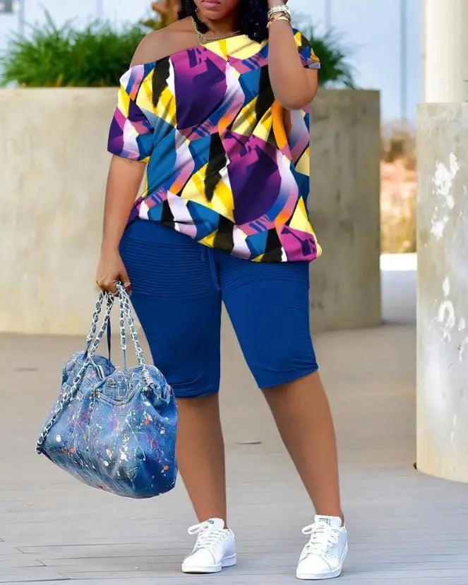 A woman wears the Womens Two Piece Sets Outfit—an all-over melting colors print skew neck top and shorts set. She stands outdoors with a blue handbag, white sneakers, and her face partially hidden by her hand.