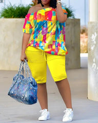 A woman models the Womens Two Piece Sets Outfit Melting Colors All Over Print Skew Neck Top & Shorts Set, styled with white sneakers and a large blue splatter tote. Her face is not shown.