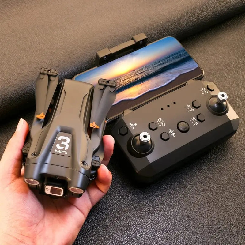 A hand holds a folded black Z908 Pro Drone Professional 4K HD Camera Mini4 Quadcopter labeled “3 Mini” next to a black remote controller and a smartphone showing a sunset over the ocean.
