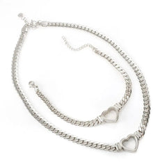 A silver-toned stainless steel jewelry set featuring a heart-shaped chain necklace and bracelet.