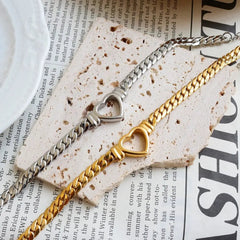 Two curb chain bracelets with heart-shaped centerpieces in gold and silver tones.