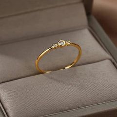The Zircon Engagement Wedding Ring for Women features a thin gold-colored stainless steel band with three cubic zirconia stones in a row, set in a minimalist design—perfect as a birthday or wedding gift. Free shipping available.
