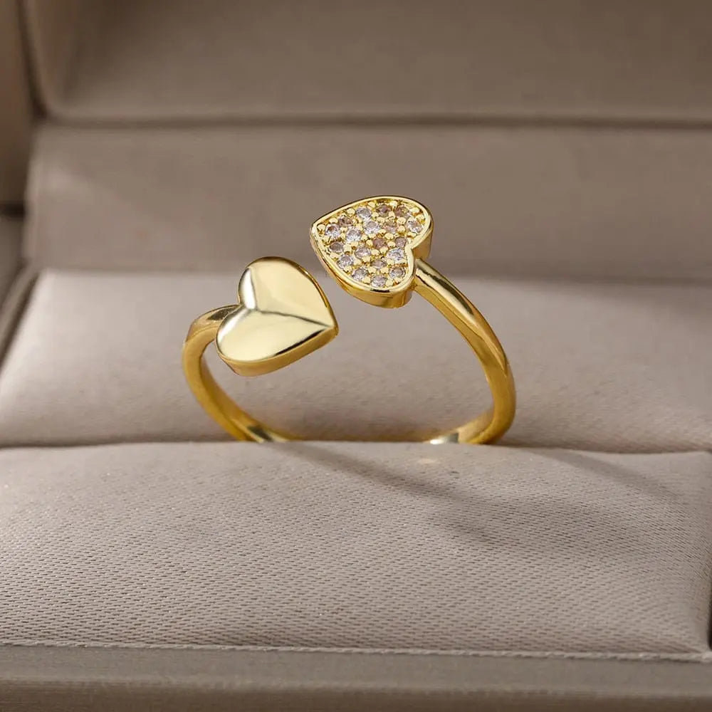 A gold color stainless steel ring for women, featuring heart-shaped ends—one solid, one with sparkling cubic zirconia—displayed on a beige jewelry box. Perfect as an engagement or wedding ring. 2023 design, free shipping.