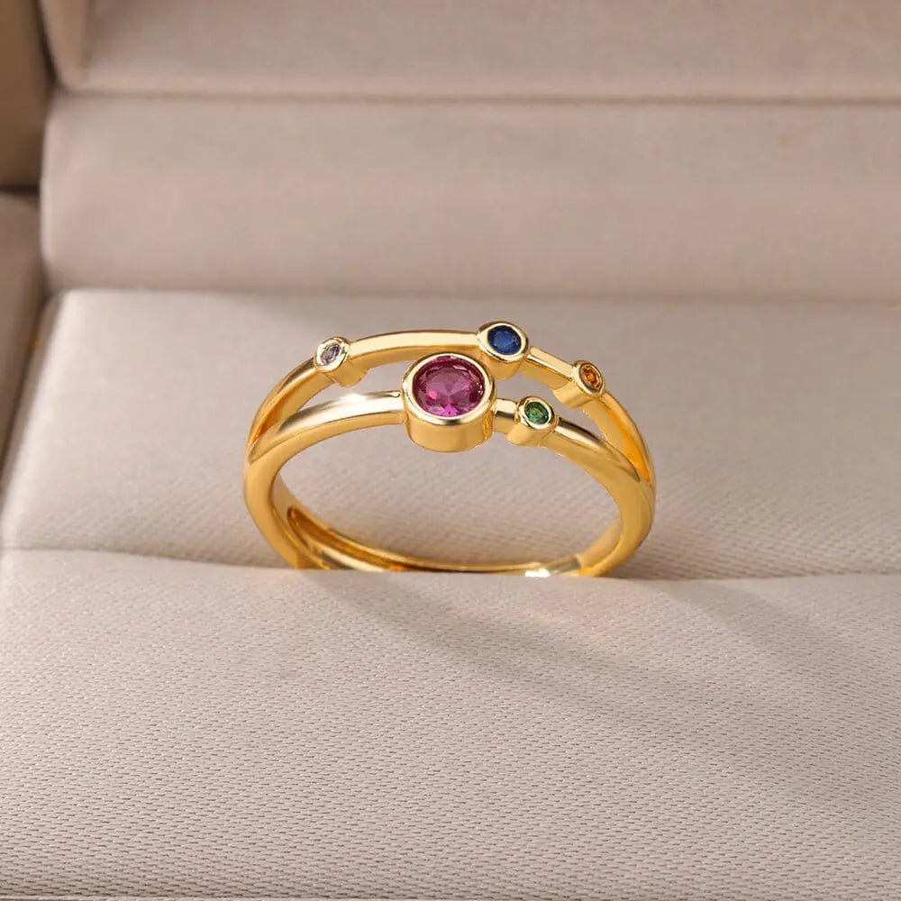 The Zircon Engagement Wedding Ring for women features a central pink gemstone with blue, green, orange, and clear Cubic Zirconia accents on gold-colored stainless steel, shown on a beige jewelry box. Ideal as a birthday gift with free shipping.