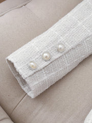 A close-up of a white tweed jacket sleeve cuff featuring three decorative pearl buttons.