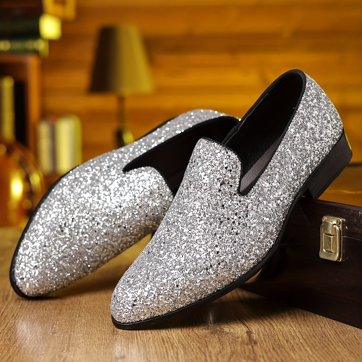 A pair of silver glittery slip-on formal shoes with a pointed toe resting on a wooden surface.