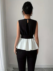 A woman wears a sleeveless black and white peplum blouse with a round neck and back keyhole.