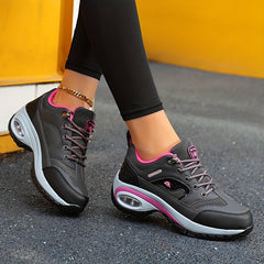 A pair of black and pink lace-up sneakers with air-cushioned soles worn on feet.