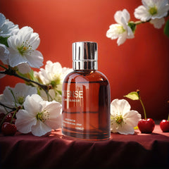 A bottle of Intense perfume sits on a red surface surrounded by white blossoms and cherries.