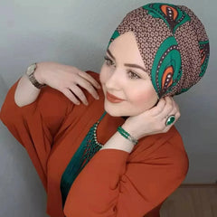 A woman wears a patterned green and brown turban-style hijab with a rust-colored top.