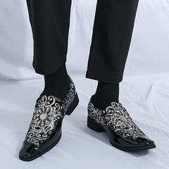 Men's black slip-on dress shoes featuring a decorative silver floral embroidery pattern.