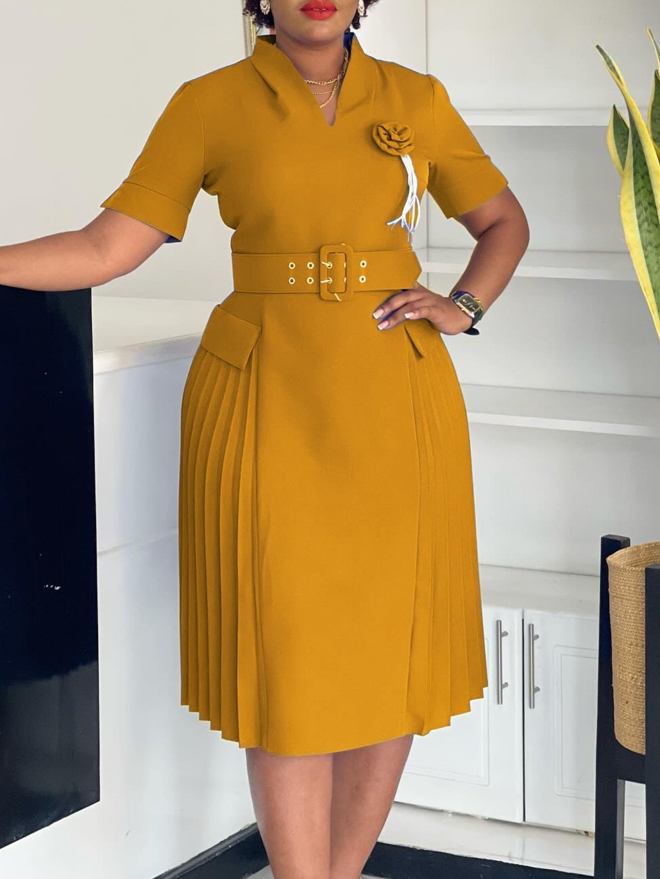 A mustard yellow V-neck dress featuring a belted waist, short sleeves, and a pleated skirt.