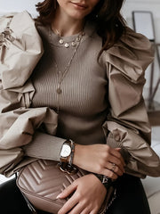 A woman wears a beige ribbed crew neck blouse featuring voluminous puff sleeves.
