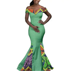 A woman wears a floor-length green mermaid dress with off-the-shoulder patterned fabric accents.