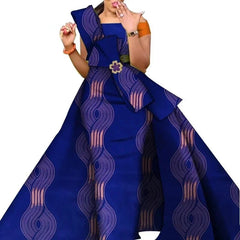 A woman wears a blue floor-length dress with a wavy pink pattern and a decorative floral brooch.