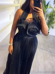 A woman wears a black sleeveless pleated two-piece set with a ruffled halter neck crop top.
