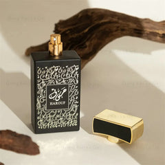 A black rectangular perfume bottle with gold Arabic calligraphy and a matching gold cap.