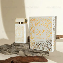 A white perfume bottle and its matching box decorated with gold Arabic calligraphy.