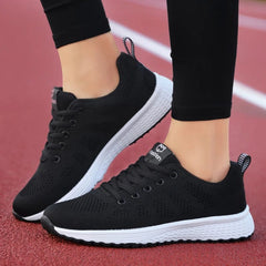A pair of black low-top lace-up sneakers with white soles worn on a red track.
