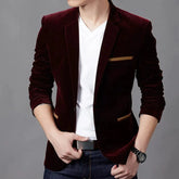 A man wears a slim-fit burgundy corduroy blazer with tan pocket accents over a white v-neck shirt.