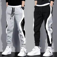 Two men wearing loose-fit, ankle-length patchwork joggers with elastic waistbands and side accents.