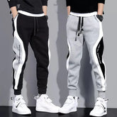 Two men wearing casual ankle-length patchwork joggers with elastic waistbands and side stripes.