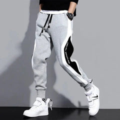 A person wears grey loose-fit joggers with black and white side panels and an elastic drawstring.