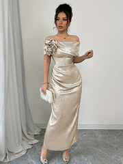 A woman wears a champagne-colored off-shoulder bodycon maxi dress with a floral accent and ruching.