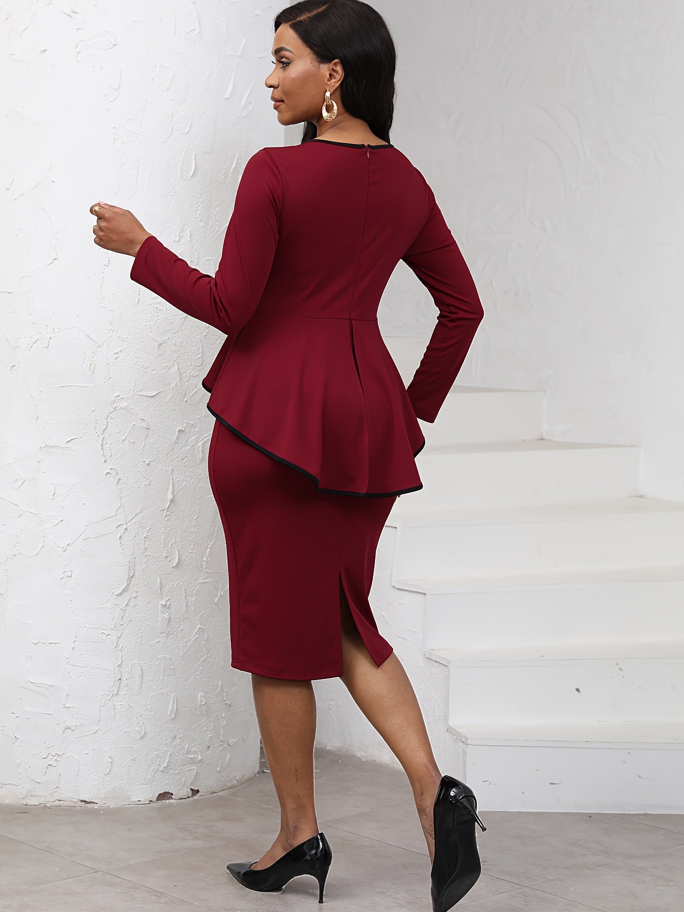 A woman wears a long-sleeved burgundy midi dress with a black-trimmed peplum waist and pencil skirt.