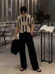 A man wears a beige short-sleeve knitted sweater with a black vertical color block pattern.