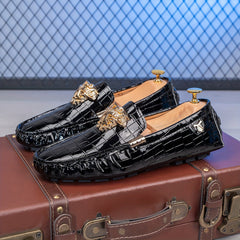 A pair of black crocodile-embossed slip-on loafers with gold Medusa-style hardware on the vamps.