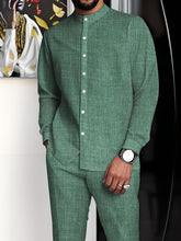 A man wears a sage green minimalist suit with a stand collar button-up shirt and matching pants.