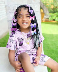 A young girl wears a purple butterfly-patterned short-sleeve top and matching shorts set.