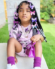 A young girl wears a matching purple butterfly-print short sleeve top and shorts set.