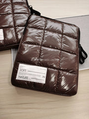 A brown quilted laptop sleeve with a minimalist white label featuring text.