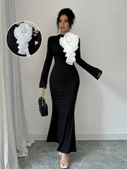 A black long-sleeve bodycon dress featuring a large white 3D pleated flower applique on the chest.