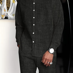 A man wears a dark grey minimalist suit with a stand collar button-up shirt and matching pants.