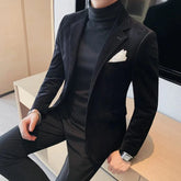 A man wears a black velvet slim-fit blazer over a matching black turtleneck sweater.