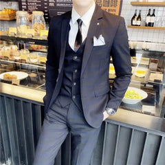 A man wears a dark three-piece suit consisting of a blazer, vest, and trousers with a white shirt.
