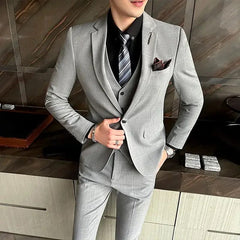 A man wears a grey plaid three-piece suit with a black shirt and a striped tie.