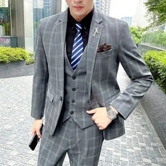 A man wearing a grey plaid three-piece suit with a black shirt and blue striped tie.