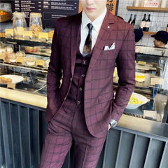 A man wears a burgundy plaid three-piece suit with a white shirt and dark tie.