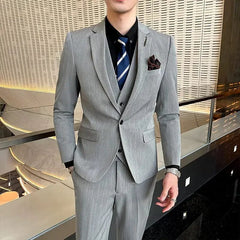 A man wears a grey pinstriped three-piece suit with a black shirt and blue striped tie.