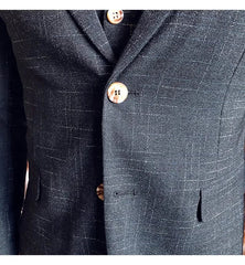 A close-up of a dark grey, single-breasted blazer featuring a subtle grid pattern and light buttons.