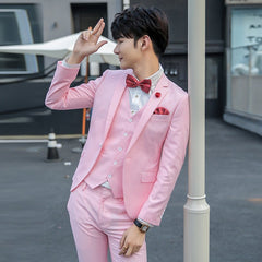 A man wears a slim-fit pink three-piece suit with a red patterned bow tie and pocket square.