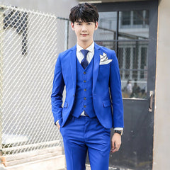 A man wears a slim-fit, solid blue three-piece suit with a white shirt and a dark blue tie.