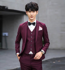 A man wears a slim-fit, solid burgundy three-piece suit with a white shirt and black bow tie.